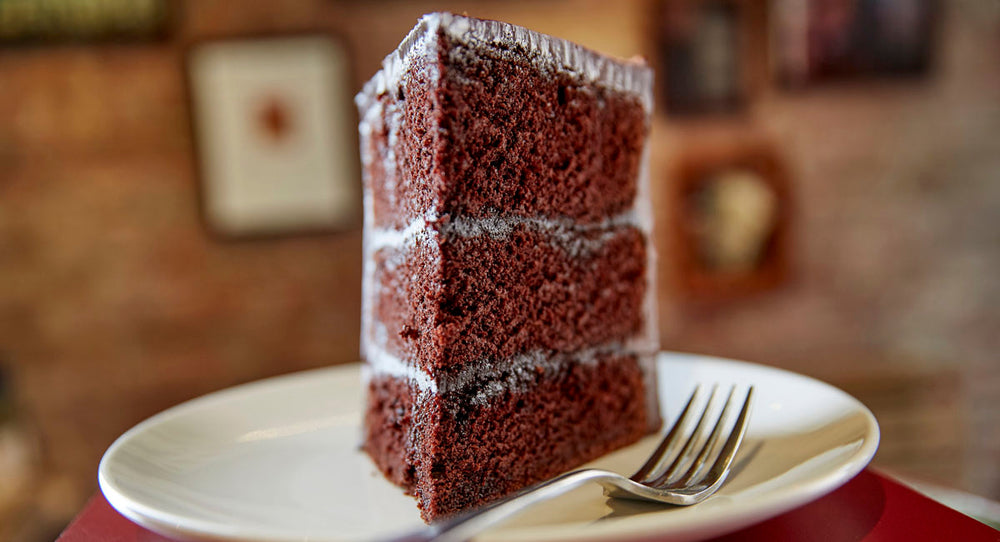 Close up looking into the point of a slice of chocolate layer cake - on a plate with a fork, blurred background